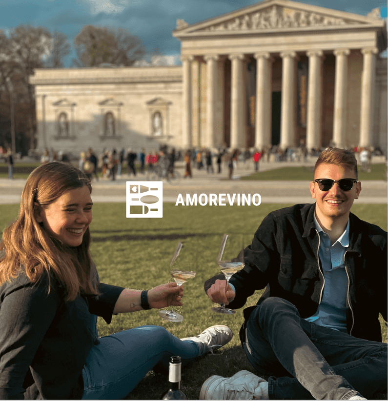 amorevino logo with two smiling people sitting on the lawn and drinking wine in front of a historic building